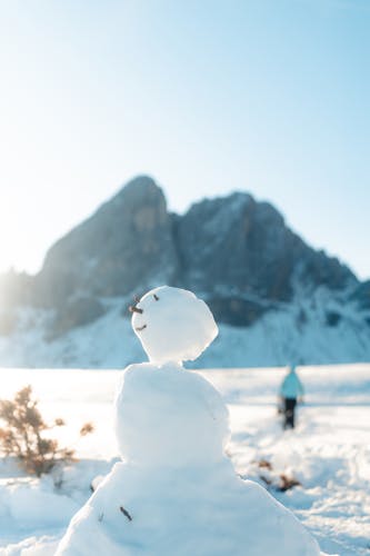 A cheerful snowman stands in a snowy field with a majestic mountain in the background.