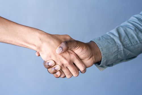 Close-up of a handshake between two people against a blue backdrop.